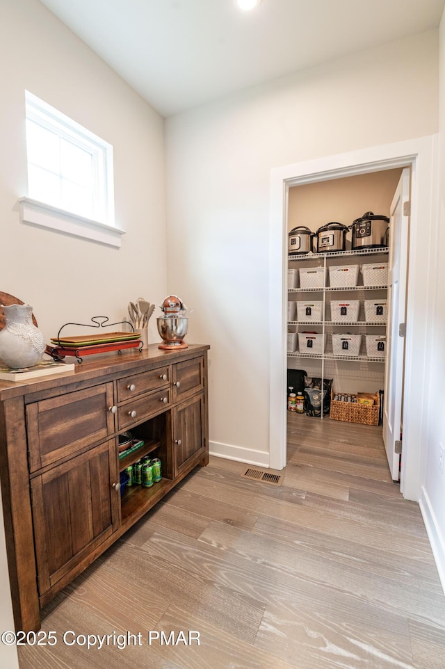 bar with dark brown cabinetry and light wood-type flooring