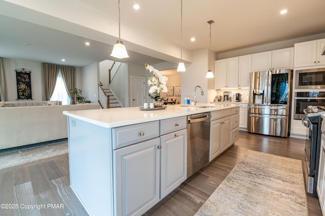 kitchen with pendant lighting, sink, appliances with stainless steel finishes, a kitchen island with sink, and white cabinets