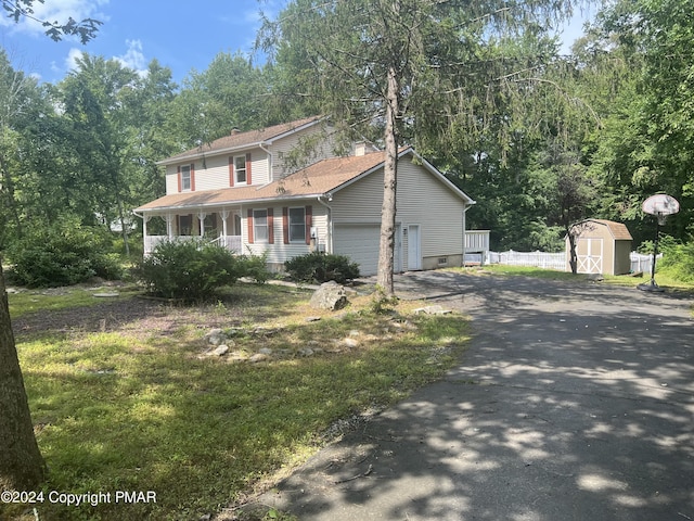 view of front facade with a storage unit, aphalt driveway, covered porch, an attached garage, and a chimney