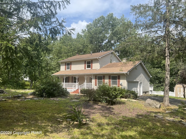 view of front of property featuring a storage unit, covered porch, a shingled roof, and a garage