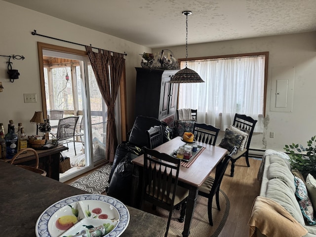 dining space featuring wood finished floors, a baseboard radiator, and a textured ceiling