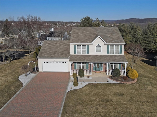 traditional-style house featuring a front yard, decorative driveway, covered porch, and an attached garage