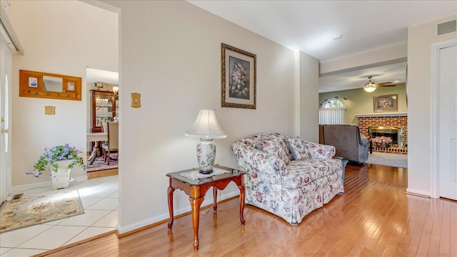 living area with a brick fireplace, baseboards, visible vents, and light wood finished floors