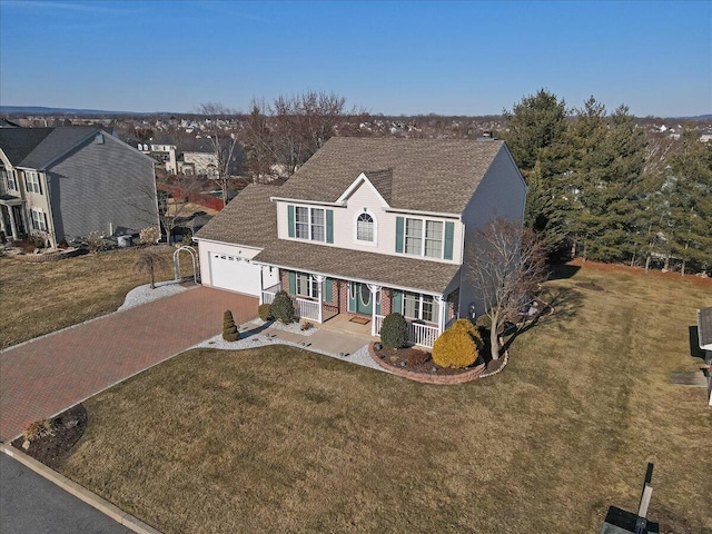 traditional home featuring decorative driveway, an attached garage, covered porch, and a front yard