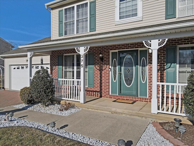 view of exterior entry featuring a garage, brick siding, and a porch