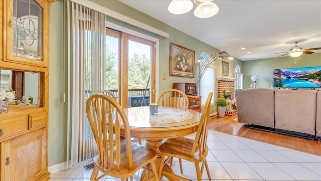 dining space featuring a fireplace, light tile patterned floors, a ceiling fan, and baseboards