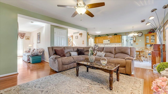 living area featuring ceiling fan with notable chandelier, visible vents, light wood-style floors, and baseboards