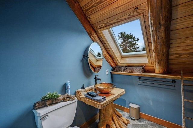 half bath with baseboards, a sink, toilet, and a skylight