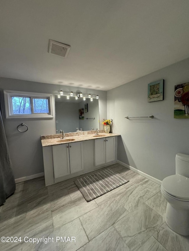 bathroom with double vanity, visible vents, toilet, a sink, and baseboards