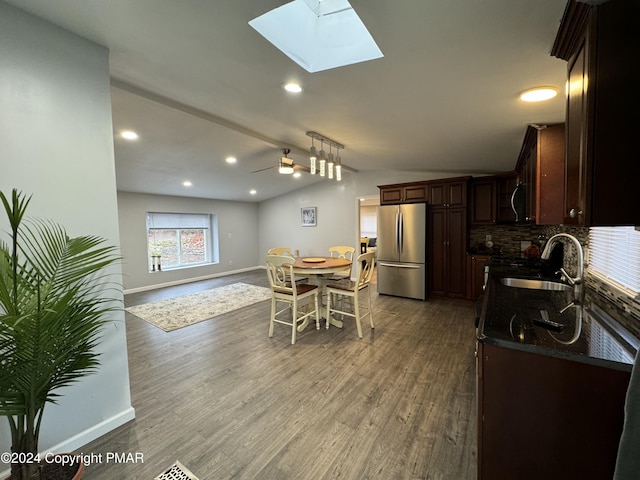 kitchen with vaulted ceiling with skylight, dark wood finished floors, freestanding refrigerator, a sink, and backsplash