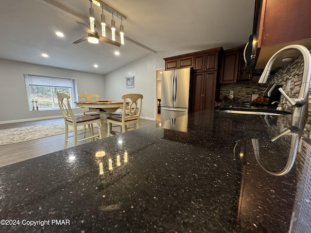 kitchen featuring vaulted ceiling with beams, baseboards, backsplash, freestanding refrigerator, and dark stone counters