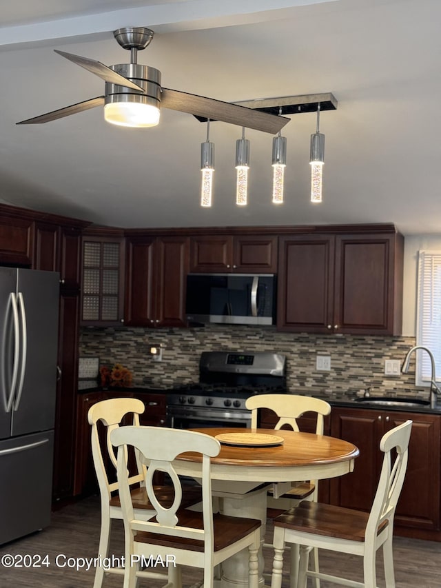 kitchen featuring dark wood-style flooring, stainless steel appliances, dark countertops, decorative backsplash, and a sink