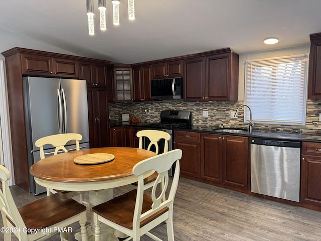 kitchen with dark countertops, backsplash, appliances with stainless steel finishes, light wood-style floors, and a sink