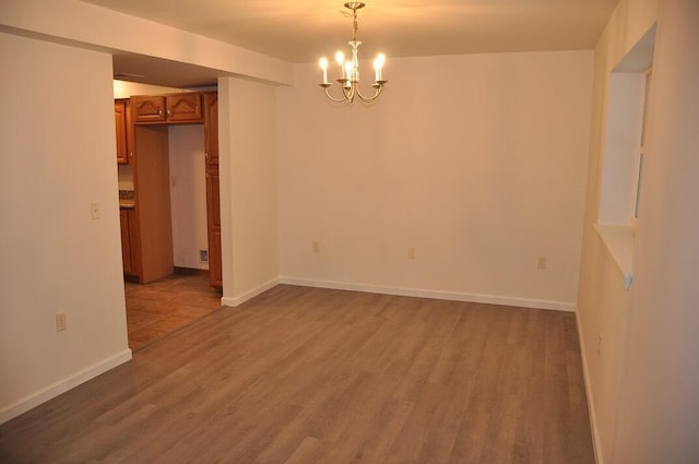 spare room with baseboards, a notable chandelier, and wood finished floors