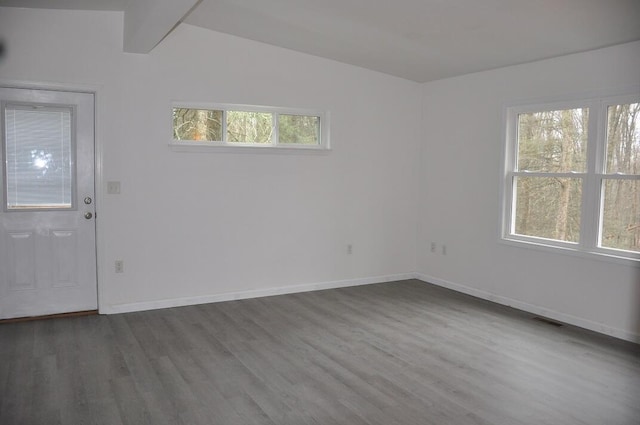 empty room featuring dark wood finished floors, visible vents, vaulted ceiling with beams, and baseboards