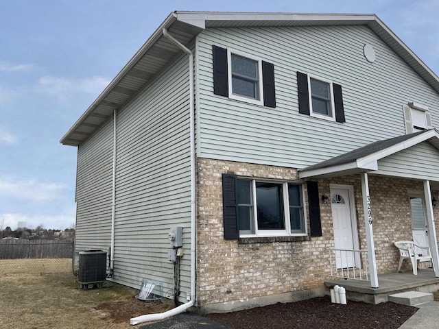 view of front of home featuring fence, brick siding, and central AC