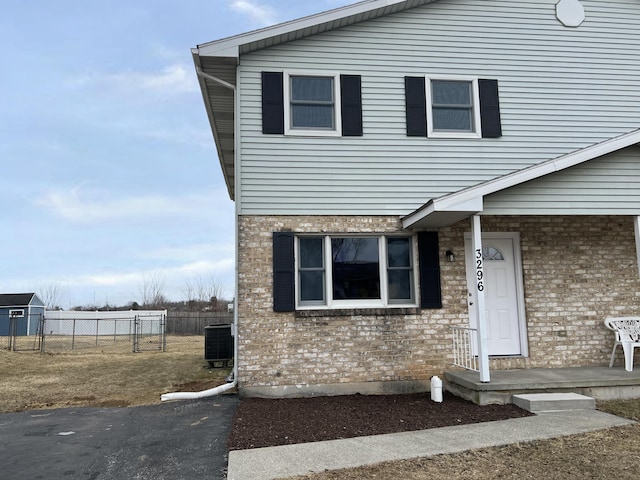 view of front facade with central AC unit, fence, and brick siding