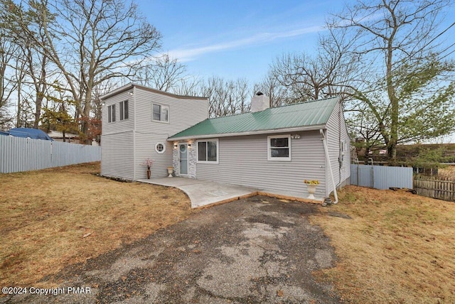 back of house with metal roof, a patio, fence, a lawn, and a chimney