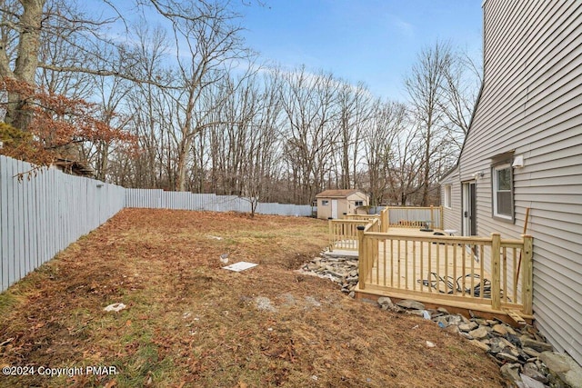 view of yard with a fenced backyard, a storage unit, a wooden deck, and an outdoor structure