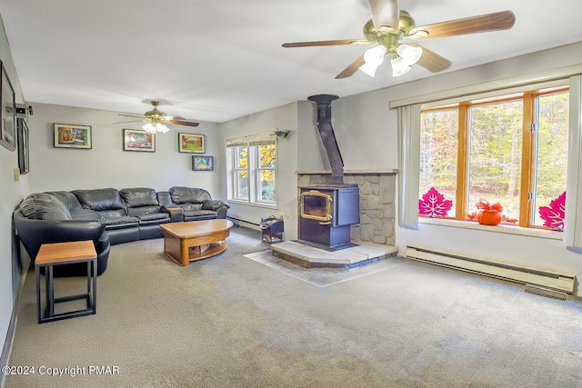 living room with a baseboard heating unit, ceiling fan, carpet flooring, and a wood stove