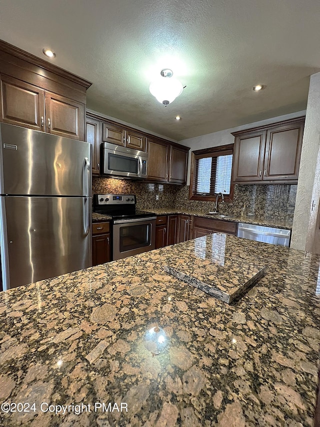 kitchen with appliances with stainless steel finishes, dark stone countertops, dark brown cabinetry, and decorative backsplash