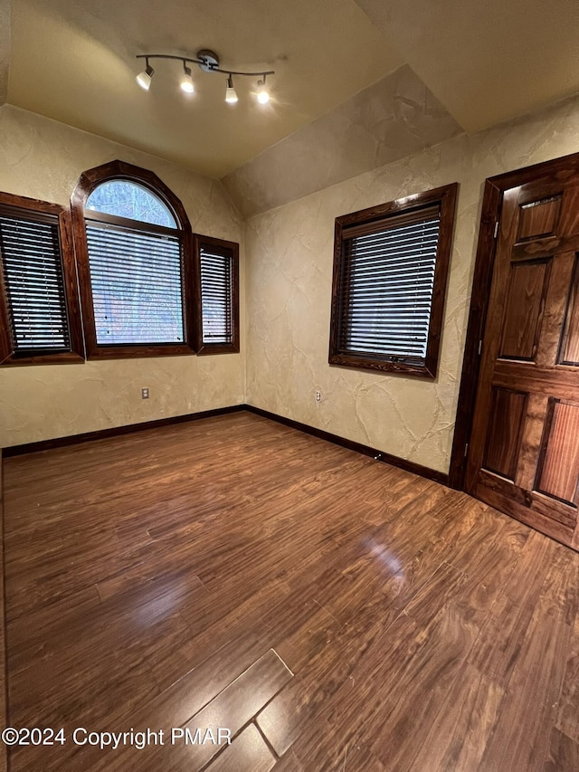 unfurnished room featuring baseboards, a textured wall, wood finished floors, vaulted ceiling, and track lighting