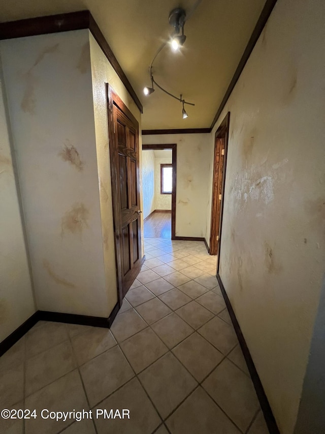 corridor with light tile patterned floors, baseboards, ornamental molding, and track lighting