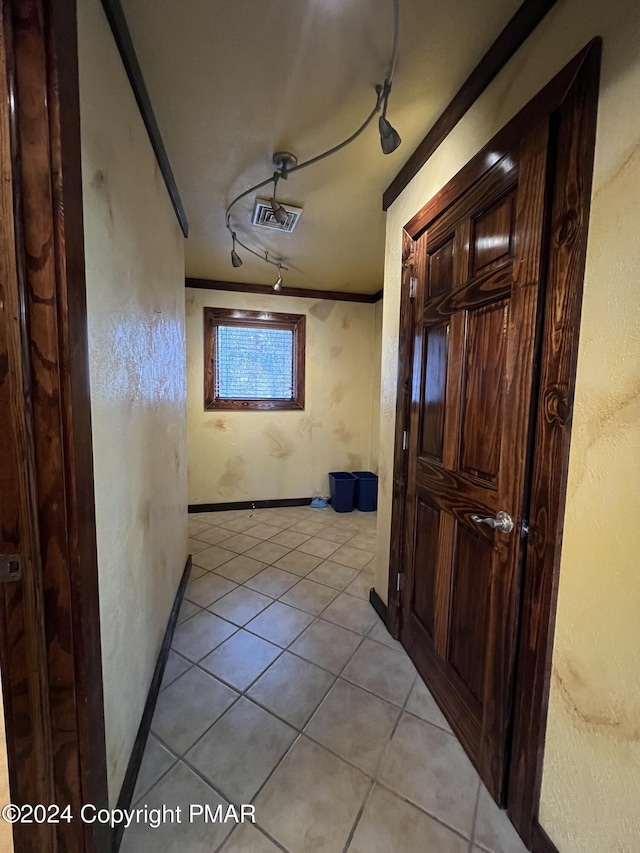 hallway with light tile patterned floors, baseboards, visible vents, crown molding, and track lighting