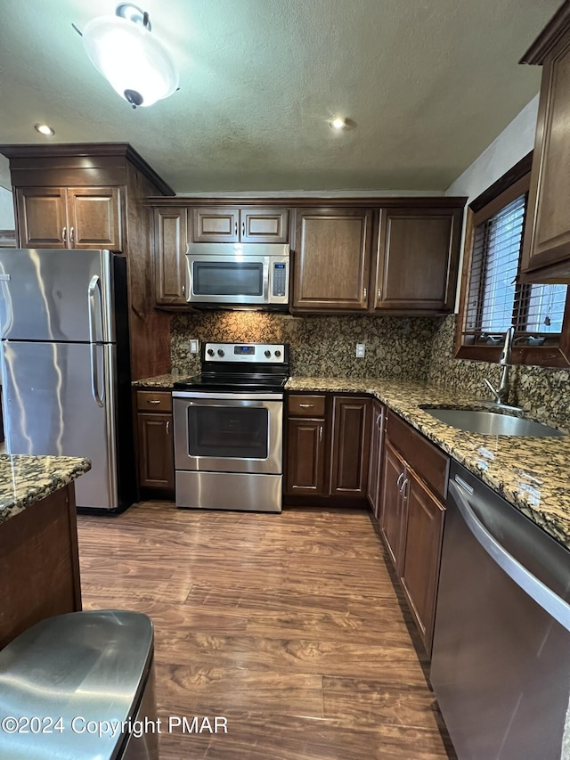 kitchen with stainless steel appliances, dark brown cabinets, dark wood-style flooring, and a sink