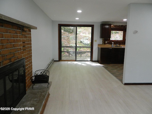 living area featuring baseboards, a baseboard radiator, light wood-type flooring, a brick fireplace, and recessed lighting