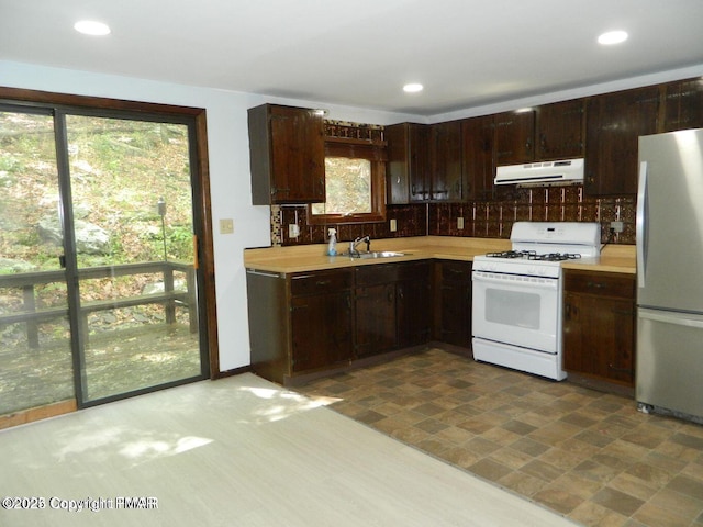 kitchen featuring exhaust hood, light countertops, freestanding refrigerator, dishwasher, and white gas range