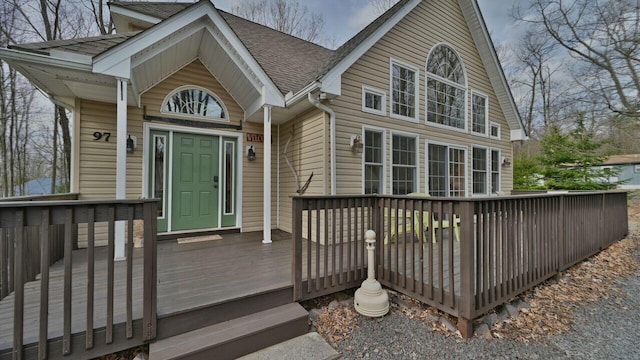entrance to property with a deck and a shingled roof