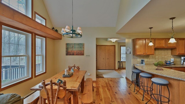 dining area with baseboards, light wood finished floors, high vaulted ceiling, and a notable chandelier