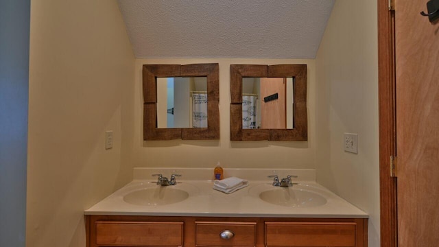 full bath with double vanity, a textured ceiling, a sink, and lofted ceiling