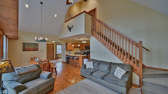 living area featuring an inviting chandelier, light wood finished floors, high vaulted ceiling, and stairway