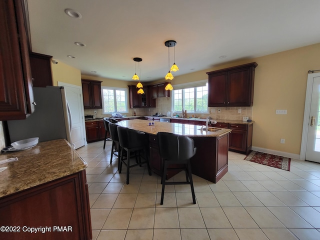 kitchen with a center island with sink, hanging light fixtures, backsplash, freestanding refrigerator, and a kitchen bar