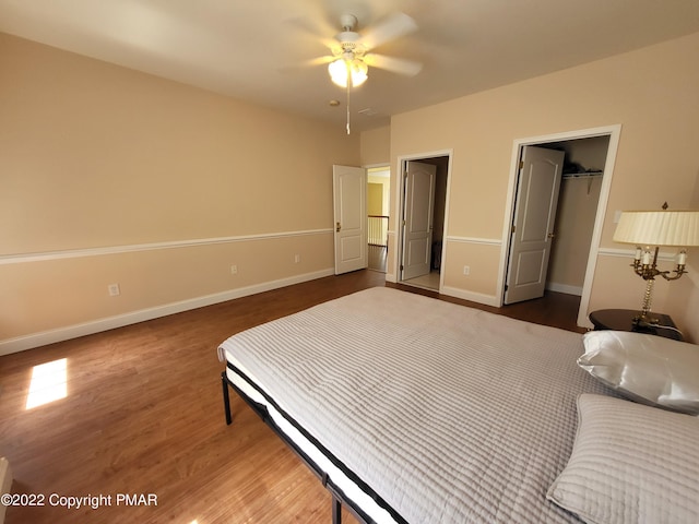 bedroom with a closet, a spacious closet, ceiling fan, wood finished floors, and baseboards