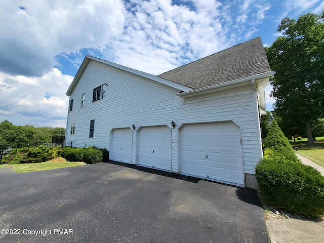 view of side of property featuring driveway and roof with shingles