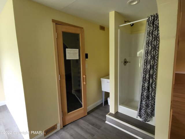 bathroom with toilet, a stall shower, baseboards, and wood finished floors