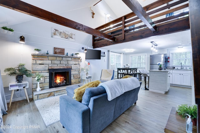 living room featuring light wood-type flooring, lofted ceiling with beams, and a stone fireplace