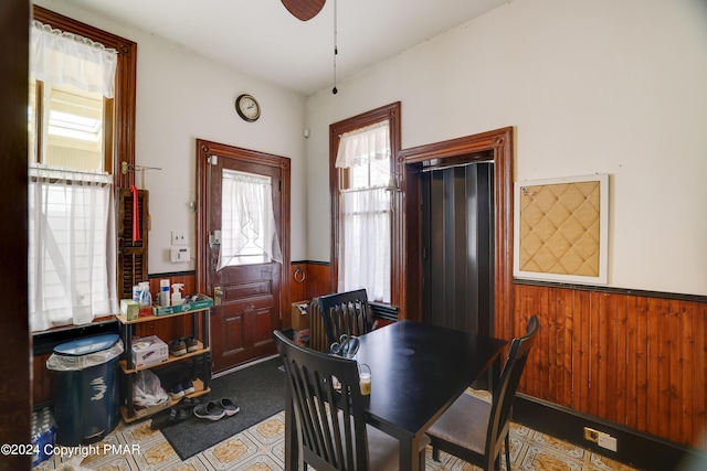 dining space with wood walls, a ceiling fan, and wainscoting