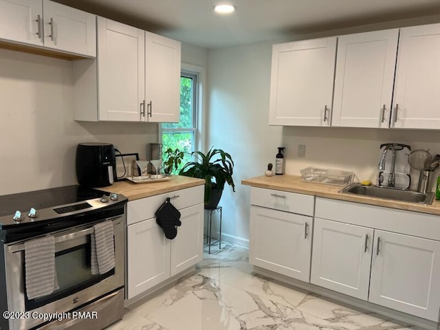 kitchen featuring butcher block countertops, stainless steel electric stove, white cabinets, and a sink