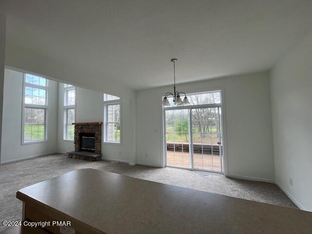 unfurnished living room featuring carpet flooring, a notable chandelier, a stone fireplace, and baseboards