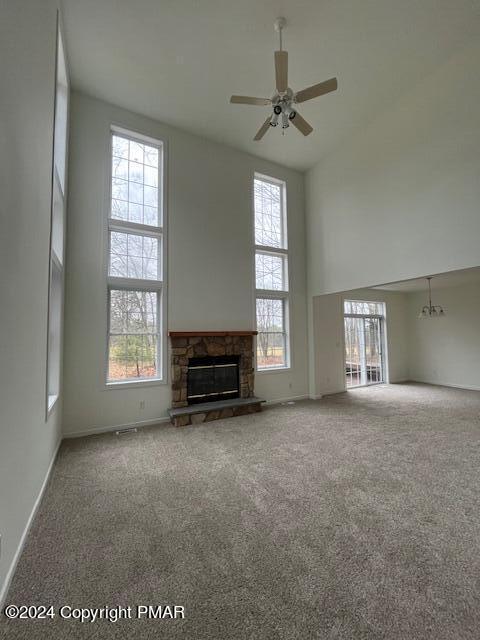 unfurnished living room with ceiling fan, a stone fireplace, a high ceiling, and carpet flooring