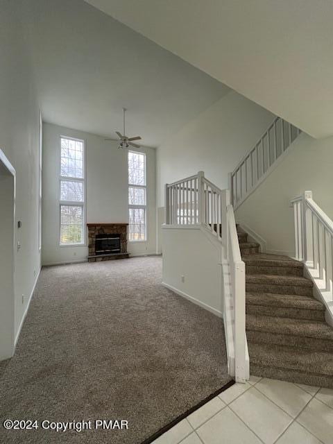 unfurnished living room featuring a fireplace, a ceiling fan, baseboards, stairs, and carpet