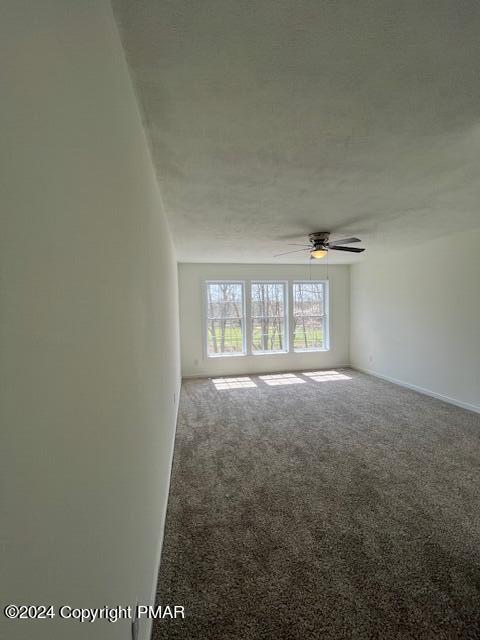 carpeted spare room featuring a ceiling fan, baseboards, and a textured ceiling