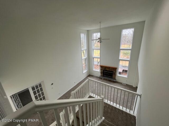 staircase featuring ceiling fan, carpet, and a fireplace with raised hearth