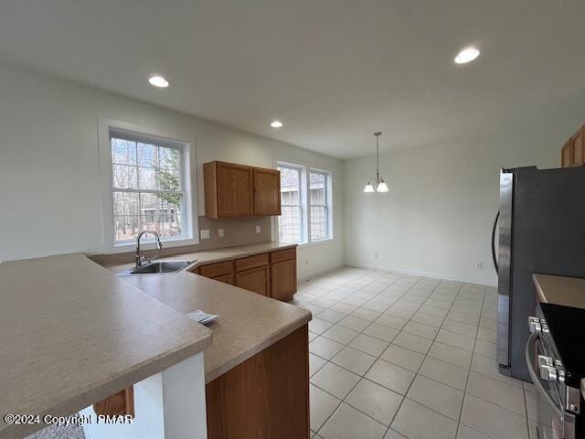 kitchen featuring brown cabinetry, freestanding refrigerator, hanging light fixtures, a sink, and recessed lighting