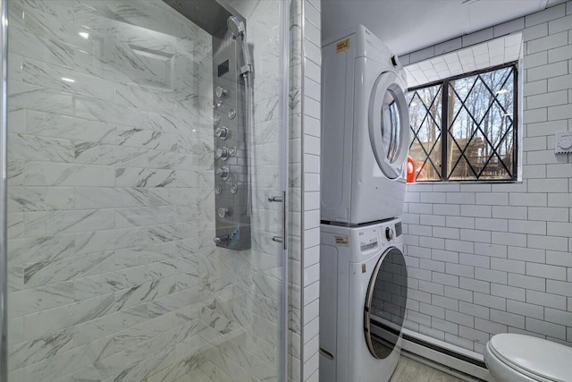 bathroom with a shower stall, stacked washer and clothes dryer, tile walls, toilet, and baseboard heating