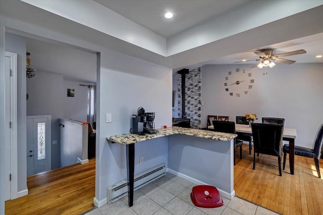 kitchen with light stone countertops, a ceiling fan, light wood finished floors, a wood stove, and a baseboard heating unit